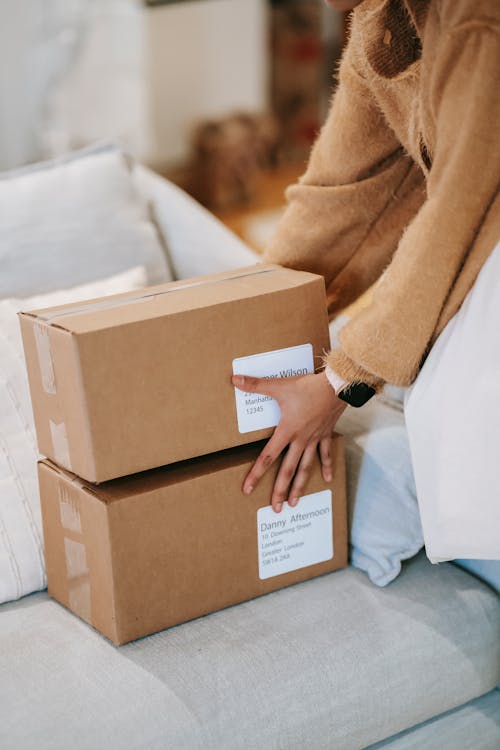 Crop anonymous female putting stack of cardboard boxes from delivery on couch at home