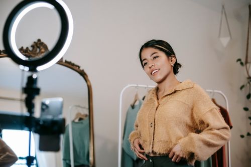 Free Low angle of positive ethnic female blogger shooting video on cellphone on tripod with shining lamp Stock Photo