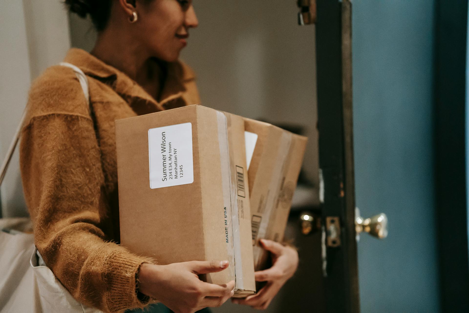 Free Crop ethnic female walking into open door of apartment with carton boxes with goods from delivery Stock Photo