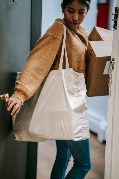Free Crop Indian woman in casual clothes with shopping bags and boxes leaving apartment and closing door Stock Photo