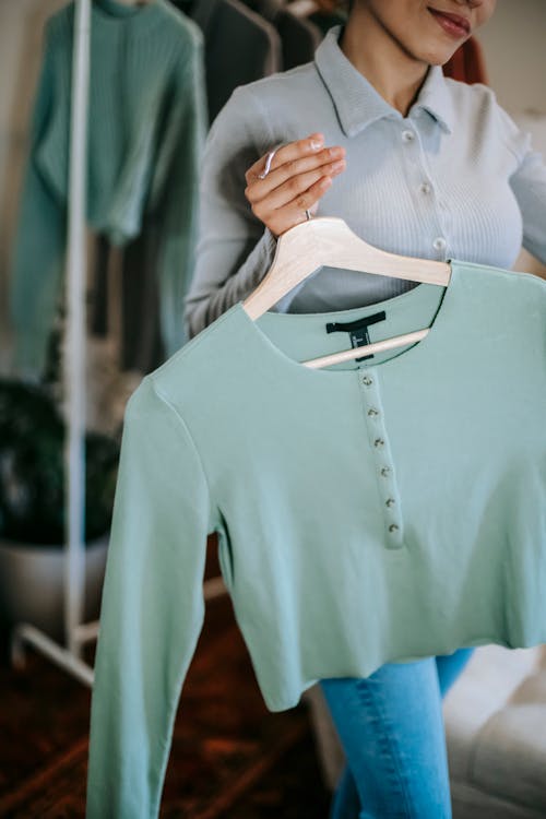 chica joven sostiene en su mano una percha con una camiseta verde