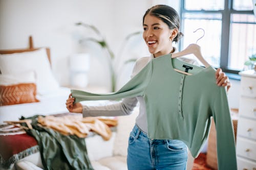 Smiling ethnic female choosing and demonstrating outfit in bedroom