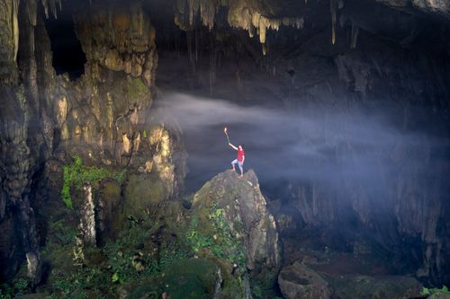 Free A lone explorer with a torch stands inside a magnificent cave in Son La, Vietnam, casting dramatic shadows. Stock Photo