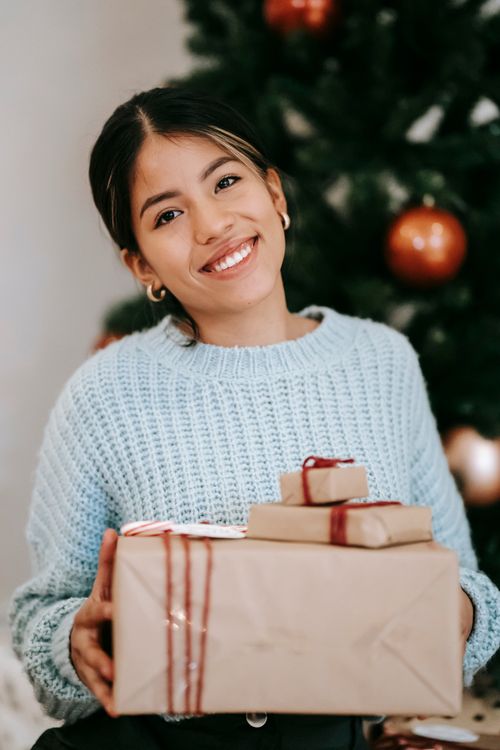 Free Content young ethnic female with present boxes looking at camera against fir tree during New Year holiday in house Stock Photo