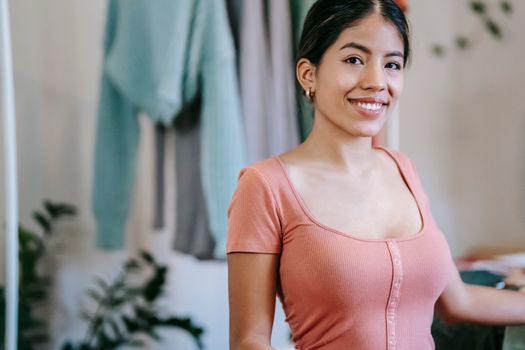 Crop young friendly ethnic female in earring looking at camera with sincere gaze at home