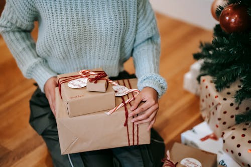 Free Crop unrecognizable female with heap of gift boxes sitting on floor during New Year holiday at home Stock Photo