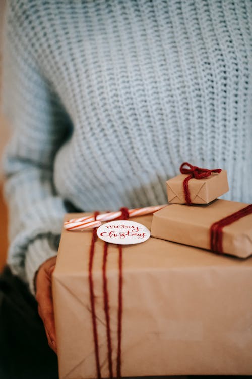 Crop unrecognizable female with heap of decorative present boxes for New Year holiday at home