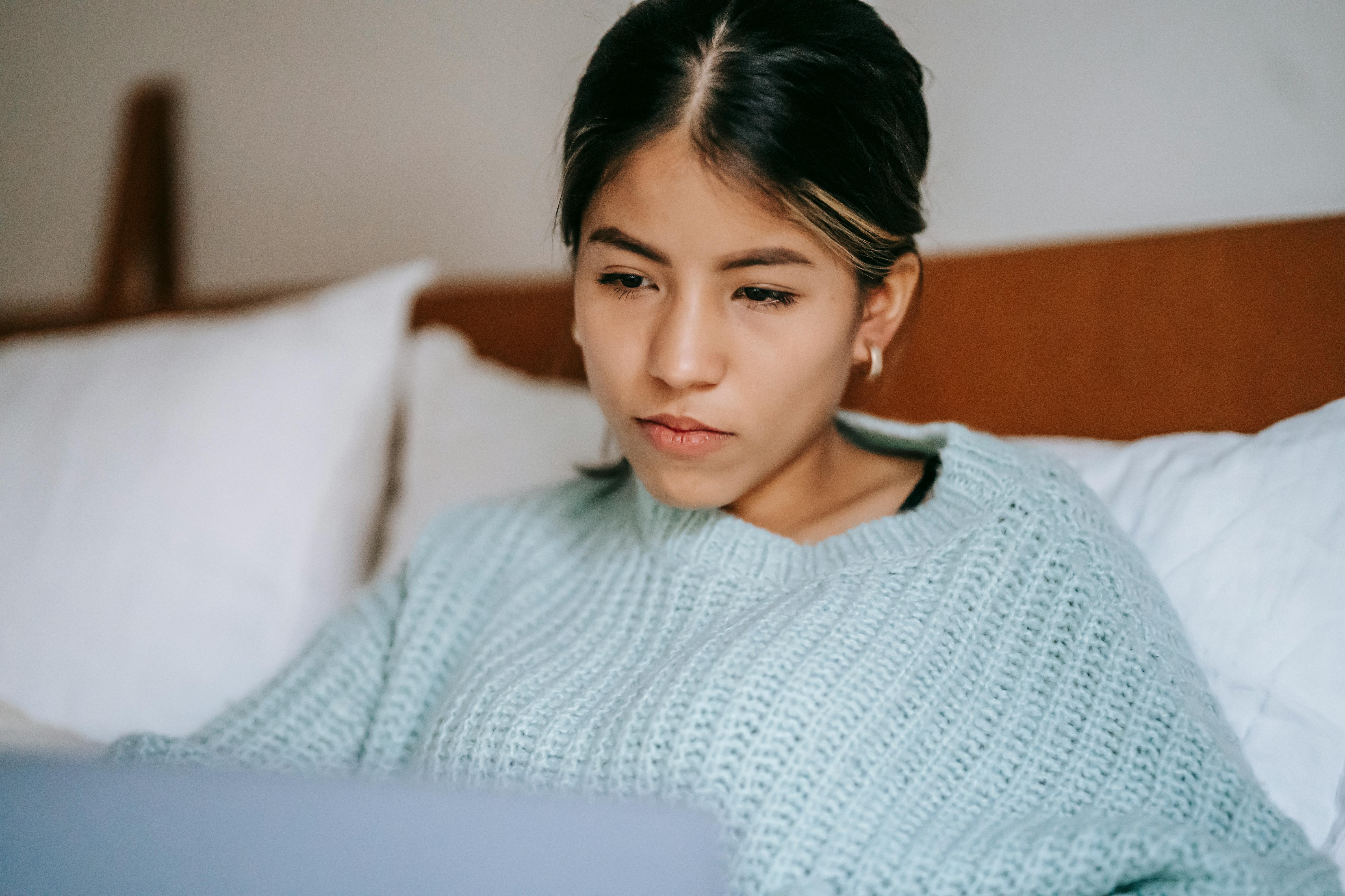 crop ethnic woman using laptop on bed in house