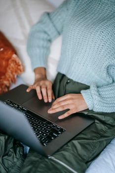 Crop anonymous female surfing internet on modern netbook while sitting on bed in house