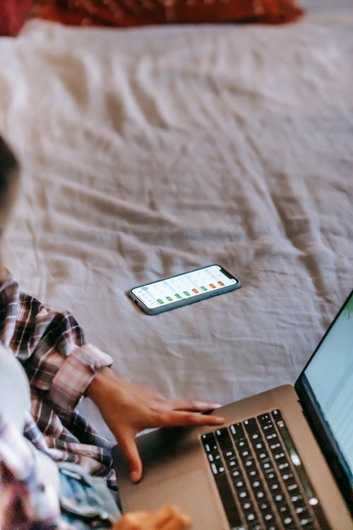 Crop freelancer working on laptop on bed