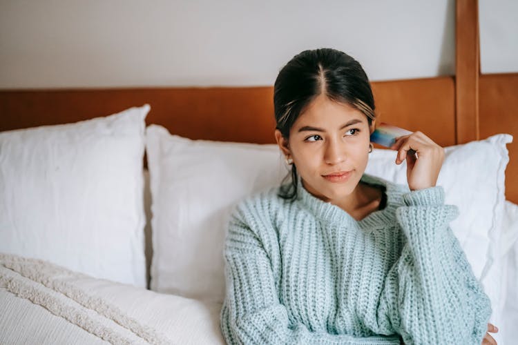 Pensive Ethnic Woman With Debit Card Resting On Bed