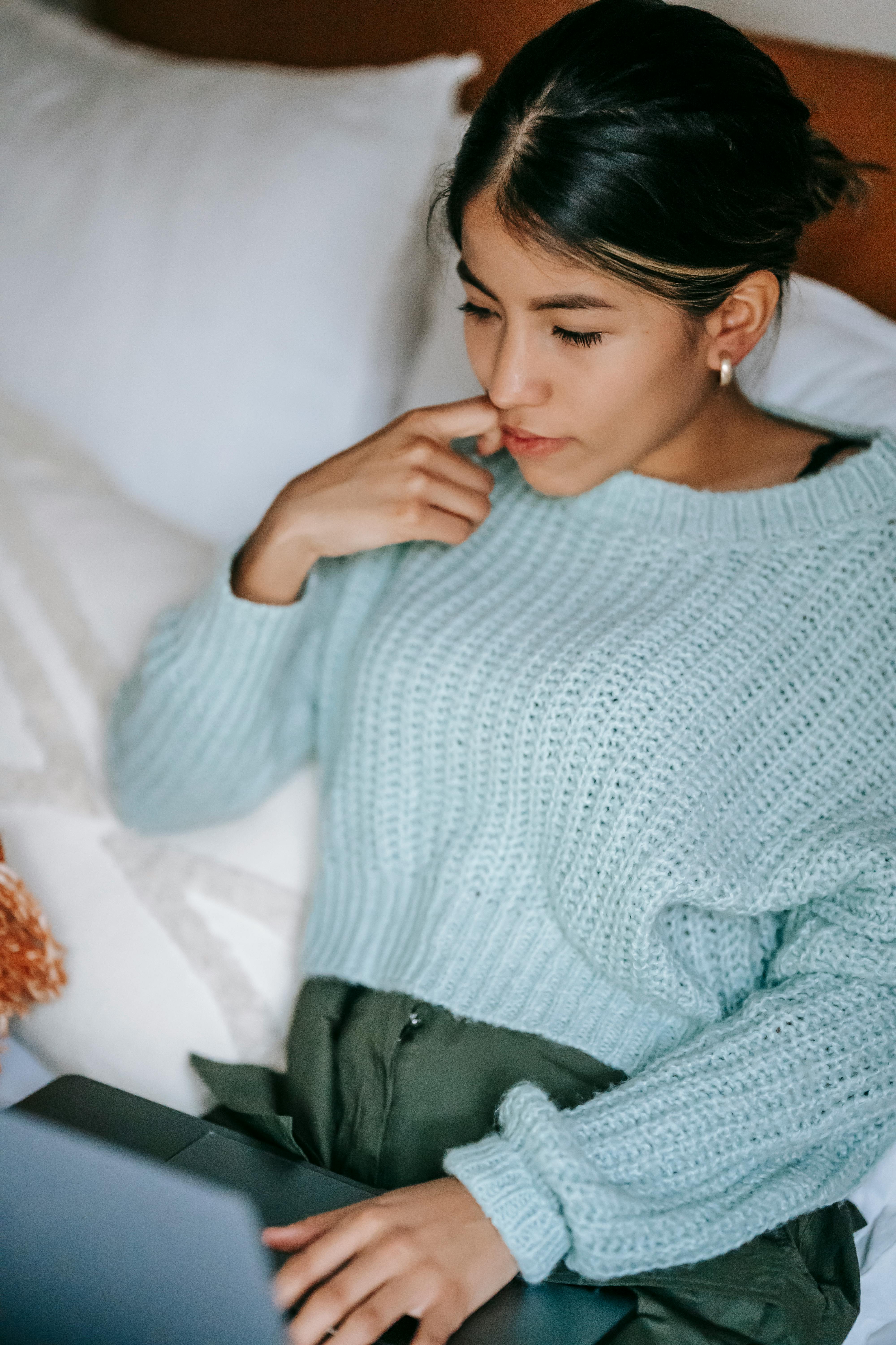 pensive ethnic woman using laptop on bed