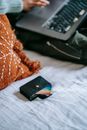 Side view of crop anonymous buyer shopping online on bed with debit card in case
