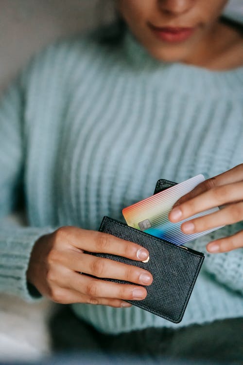 Free Crop anonymous ethnic female with credit card and leather case resting at home in daytime Stock Photo