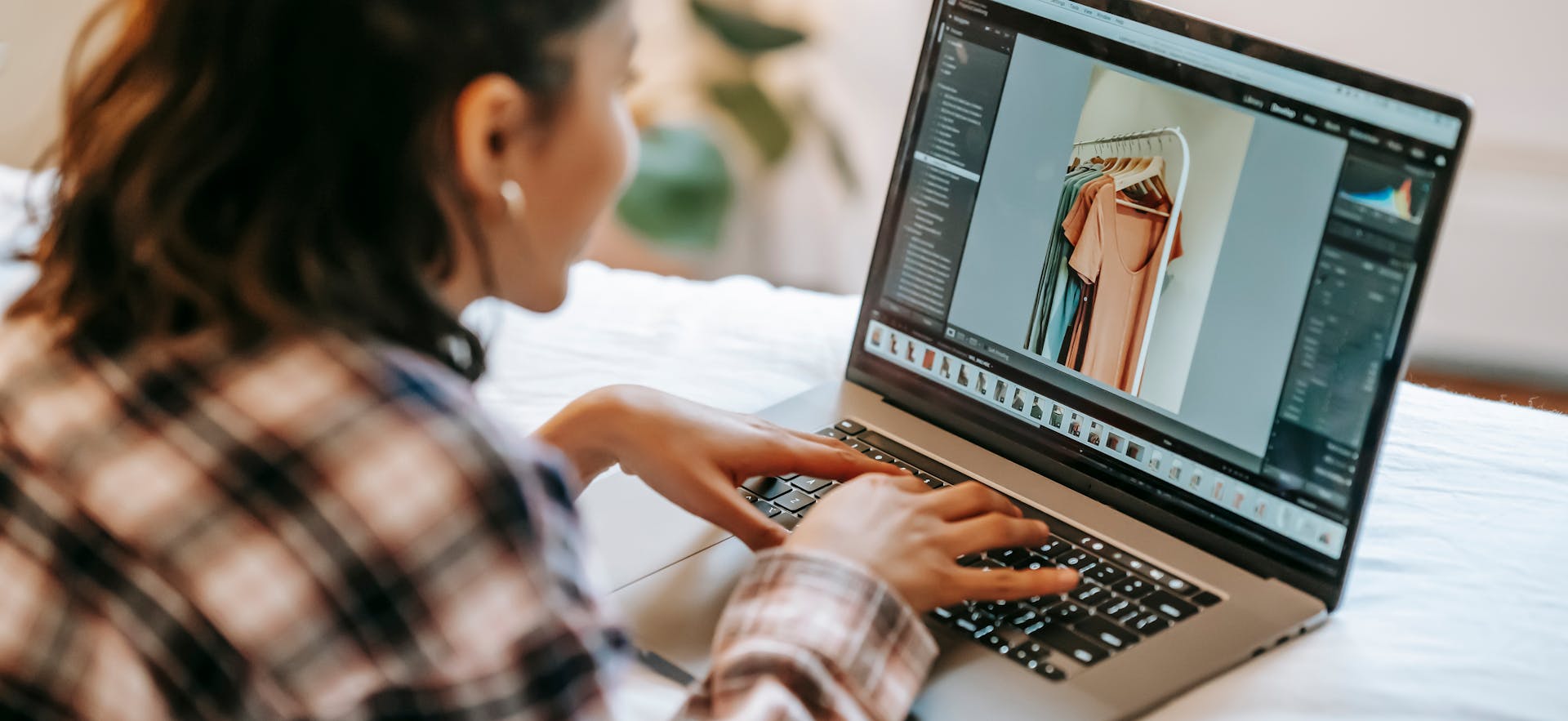 Woman editing photos on a laptop indoors, showcasing fashion items online using photo editing software.