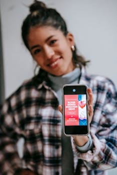 Smiling woman holding smartphone displaying blood donation drive advertisement.
