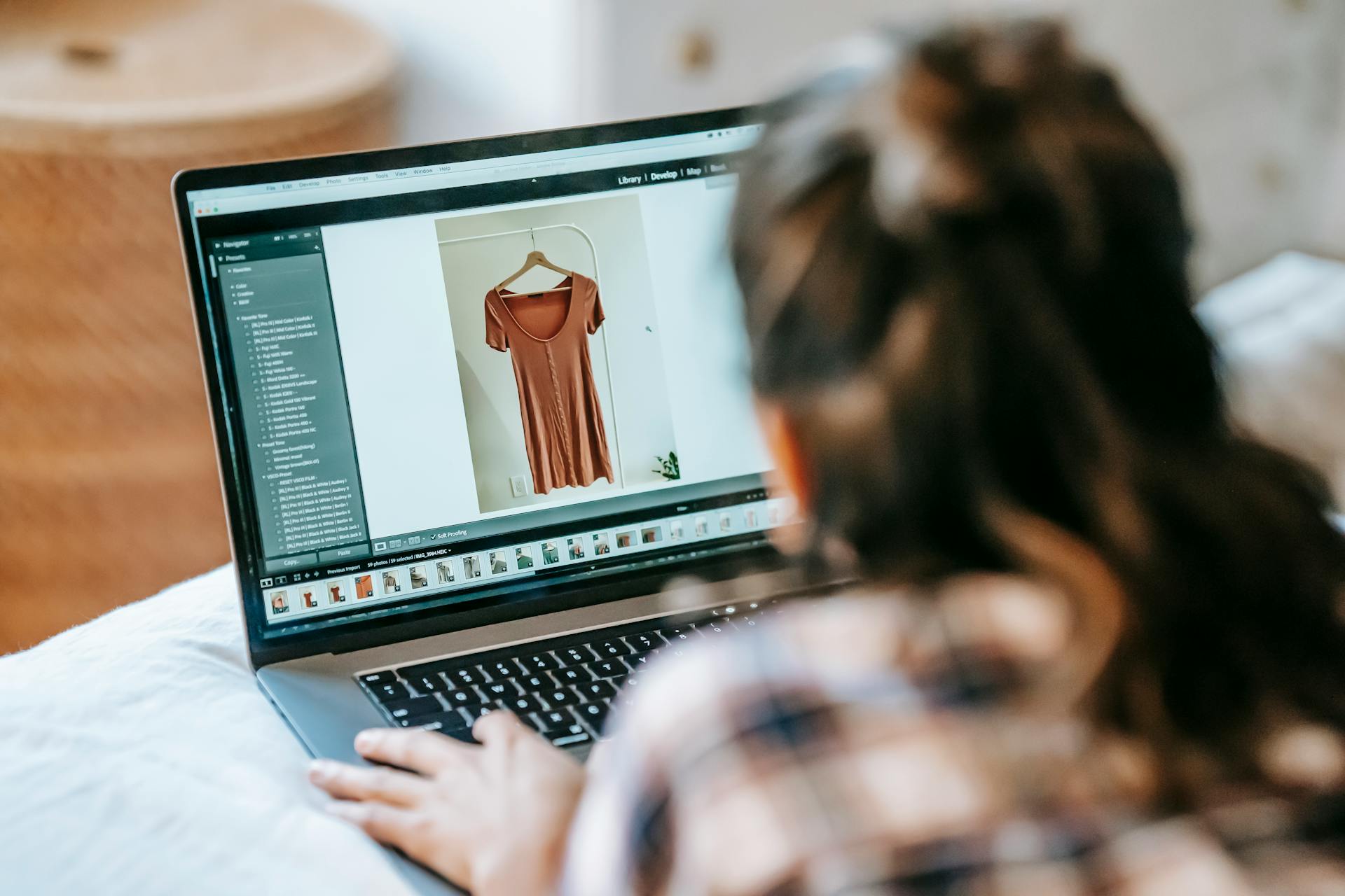 A woman edits a clothing photo on her laptop, working from home in a casual setting.