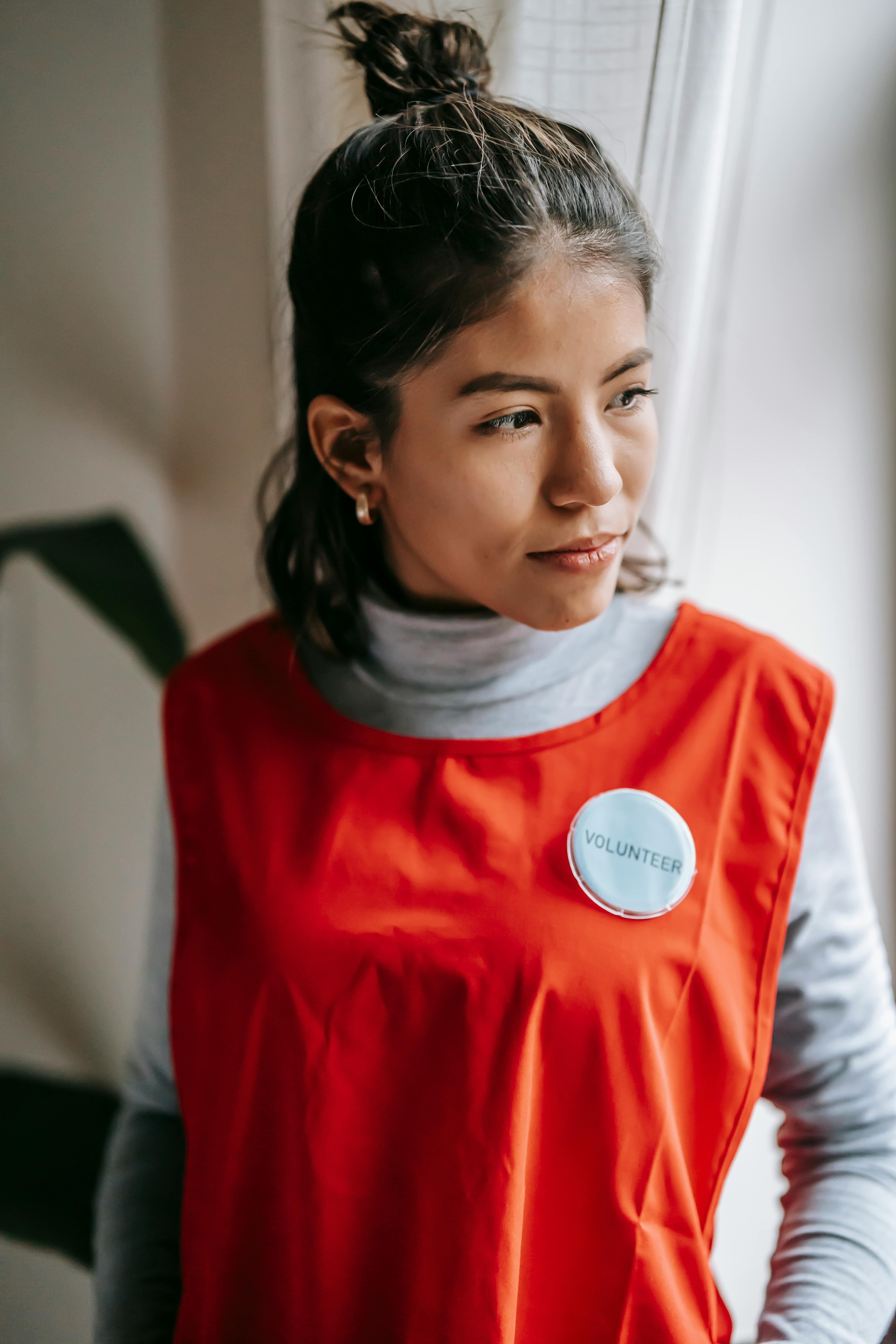 A woman volunteer wearing a red apron, gazing thoughtfully out a window.