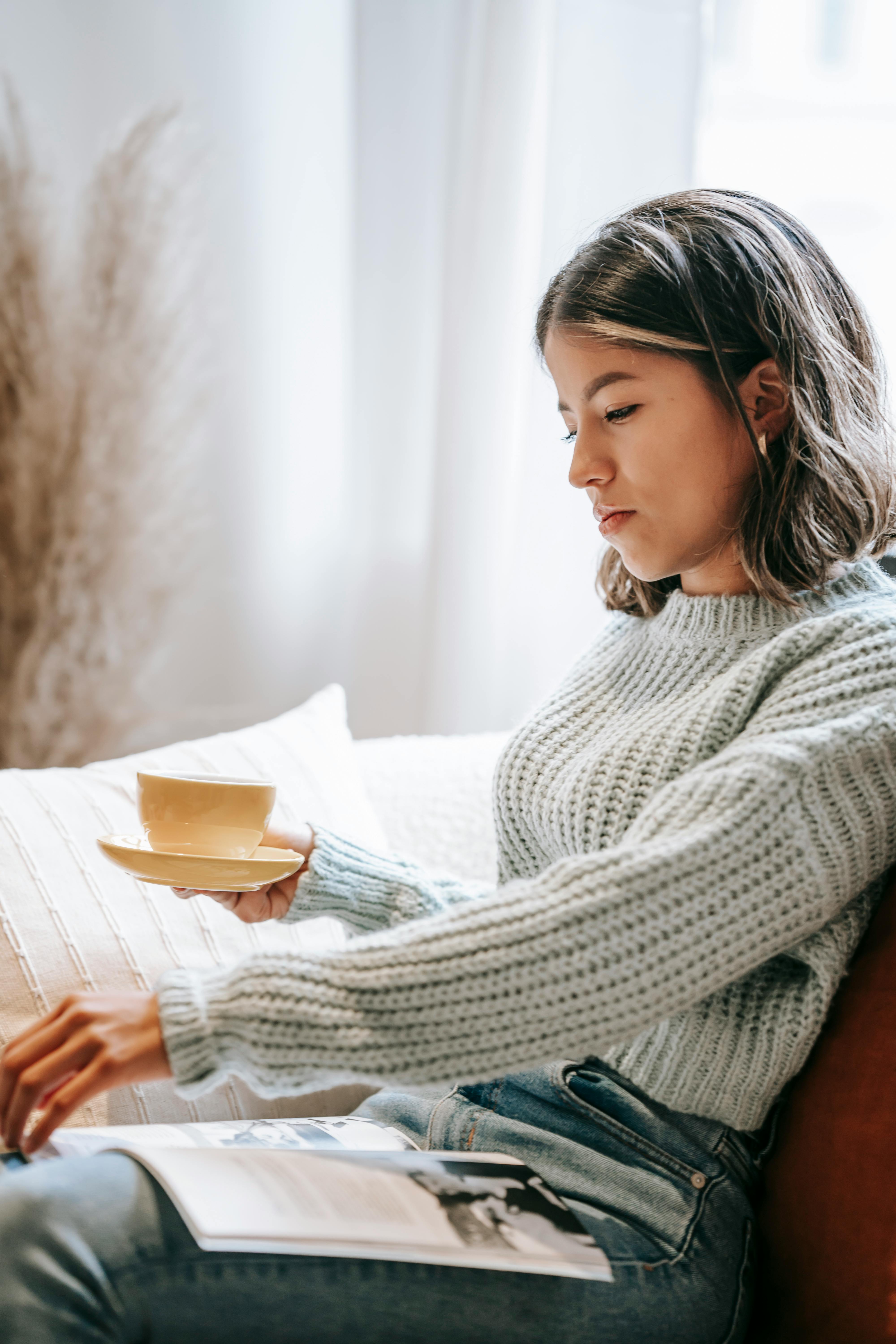 Free Side view of Asian female with mug of drink flipping page of magazine while reading with interest Stock Photo