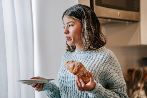 Free Serious ethnic female standing with croissant and plate Stock Photo