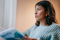 Thoughtful ethnic woman reading book in room