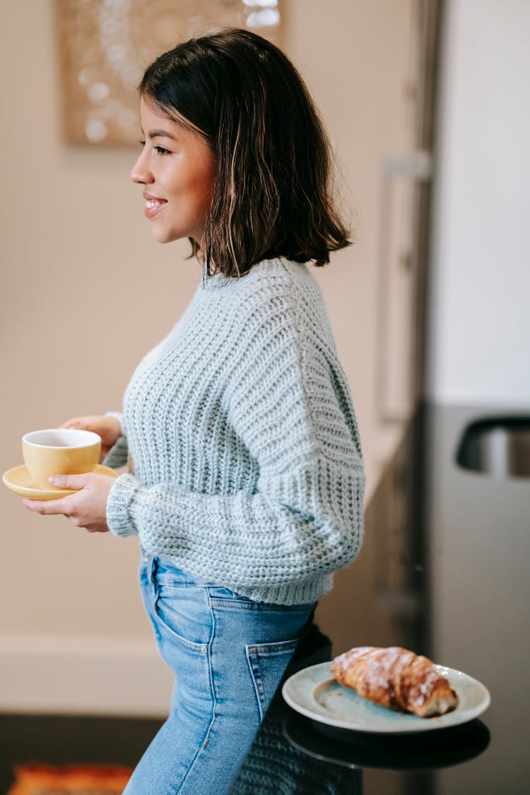 Cheerful Ethnic Woman With Cup Of Beverage In Kitchen