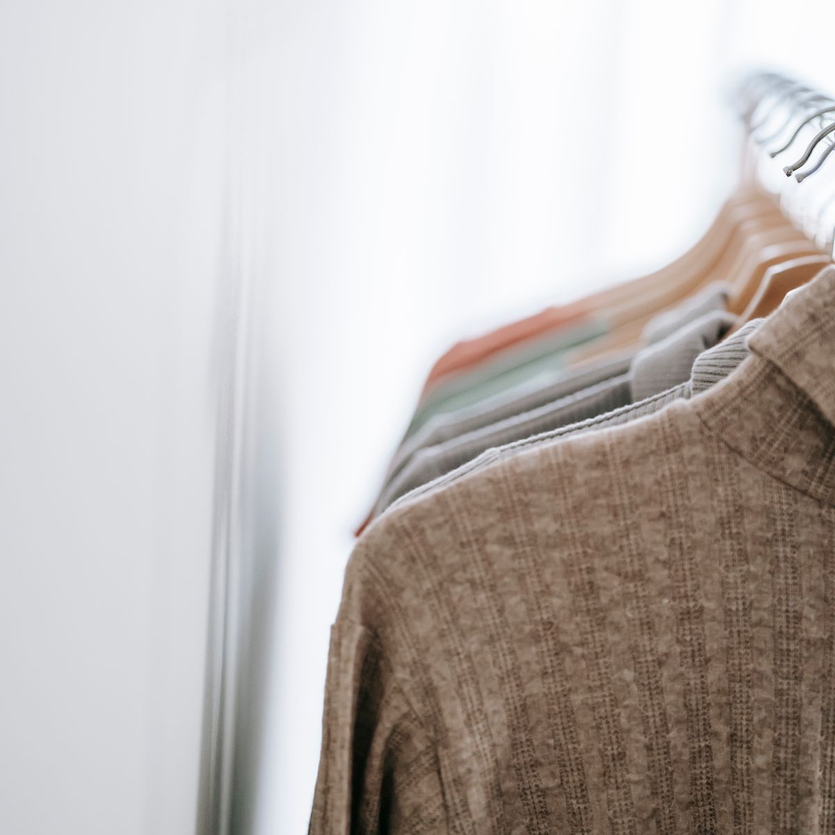 Roupas em tons neutros organizadas em cabides de madeira