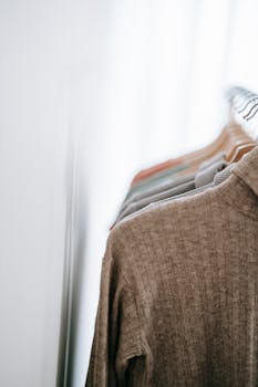 A minimalist indoor clothing rack showcasing various sweaters in a bright, blurred setting.