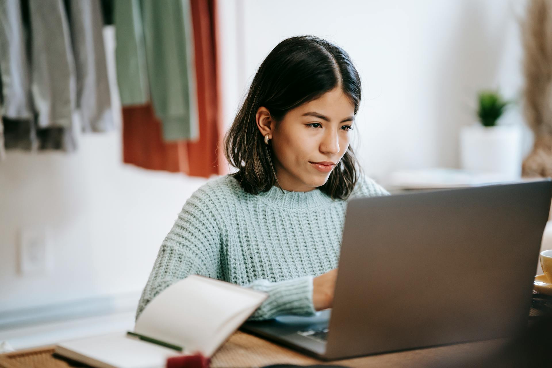 Hispanic woman working remotely on netbook near notebook at home