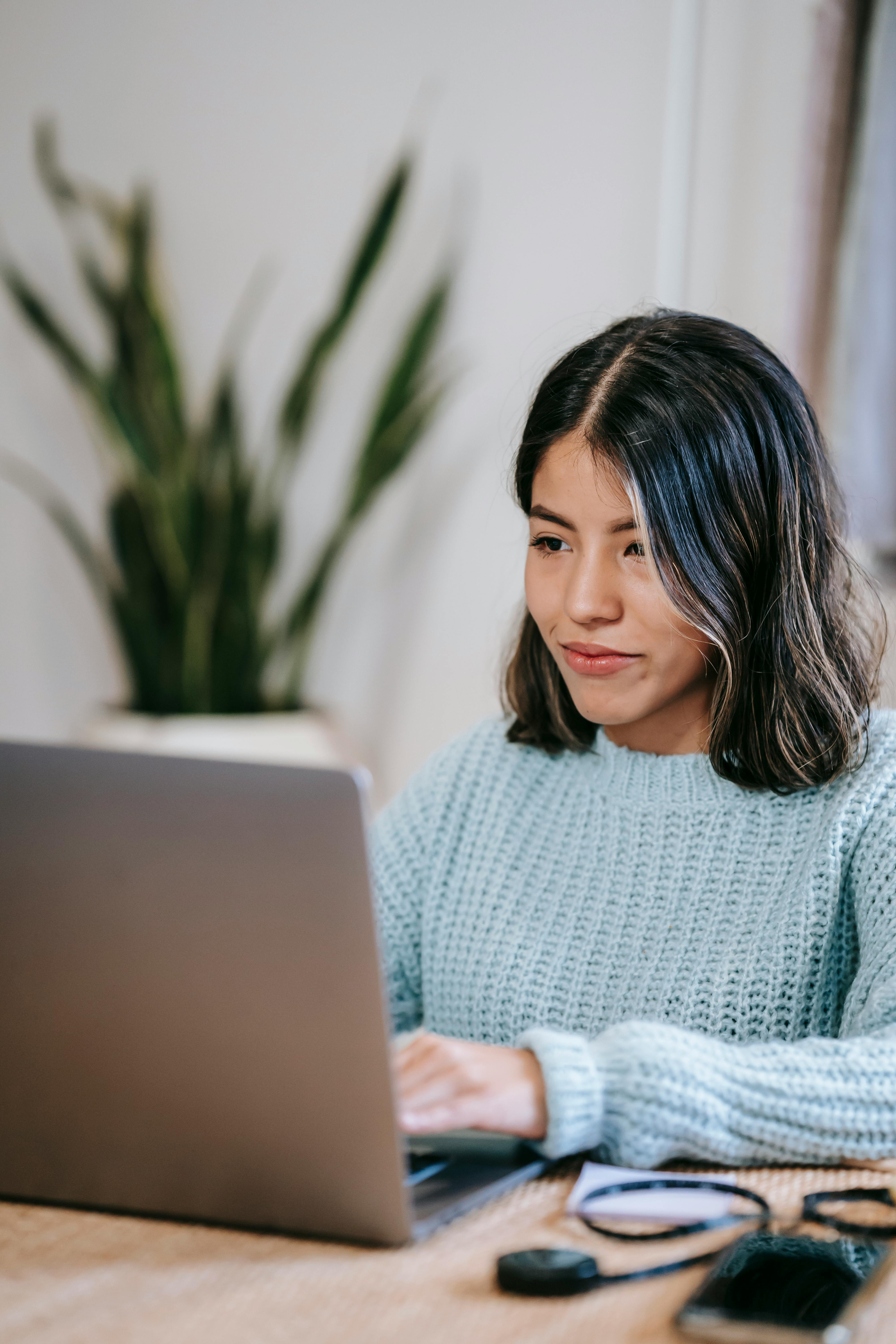 latin american female freelancer using laptop in home near plant