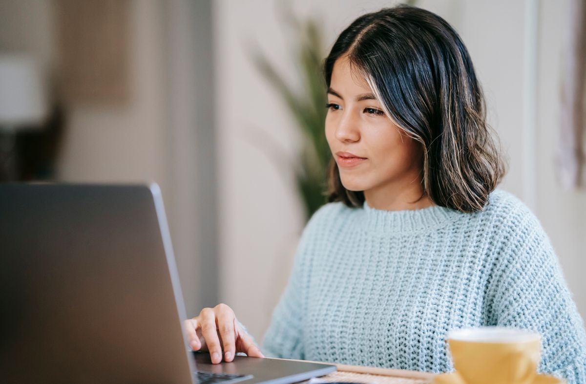 A woman using a laptop at home with a cup of tea