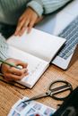 Faceless ethnic lady writing information in notepad near laptop