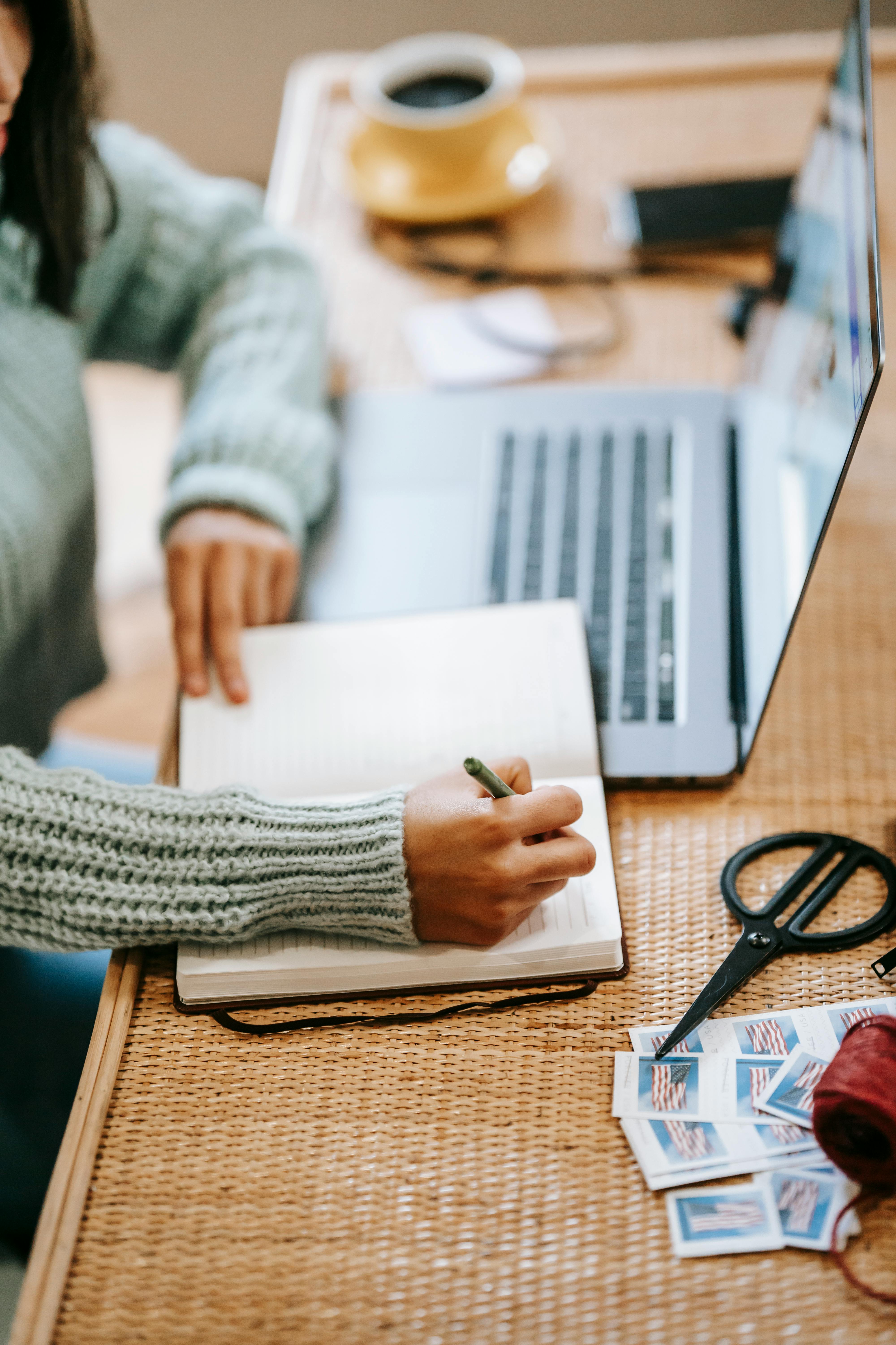 unrecognizable ethnic woman taking notes in notebook near laptop