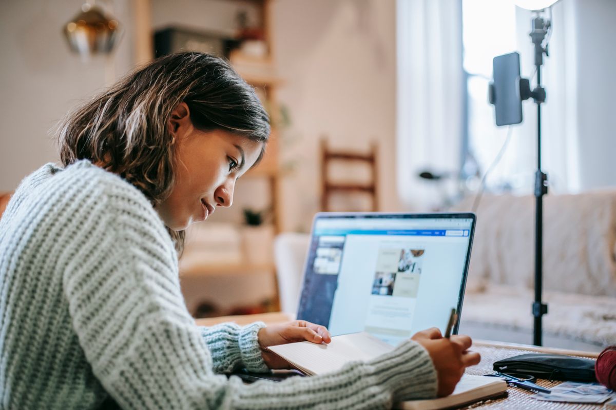 Pessoa estudando pelo computador e escrevendo anotações