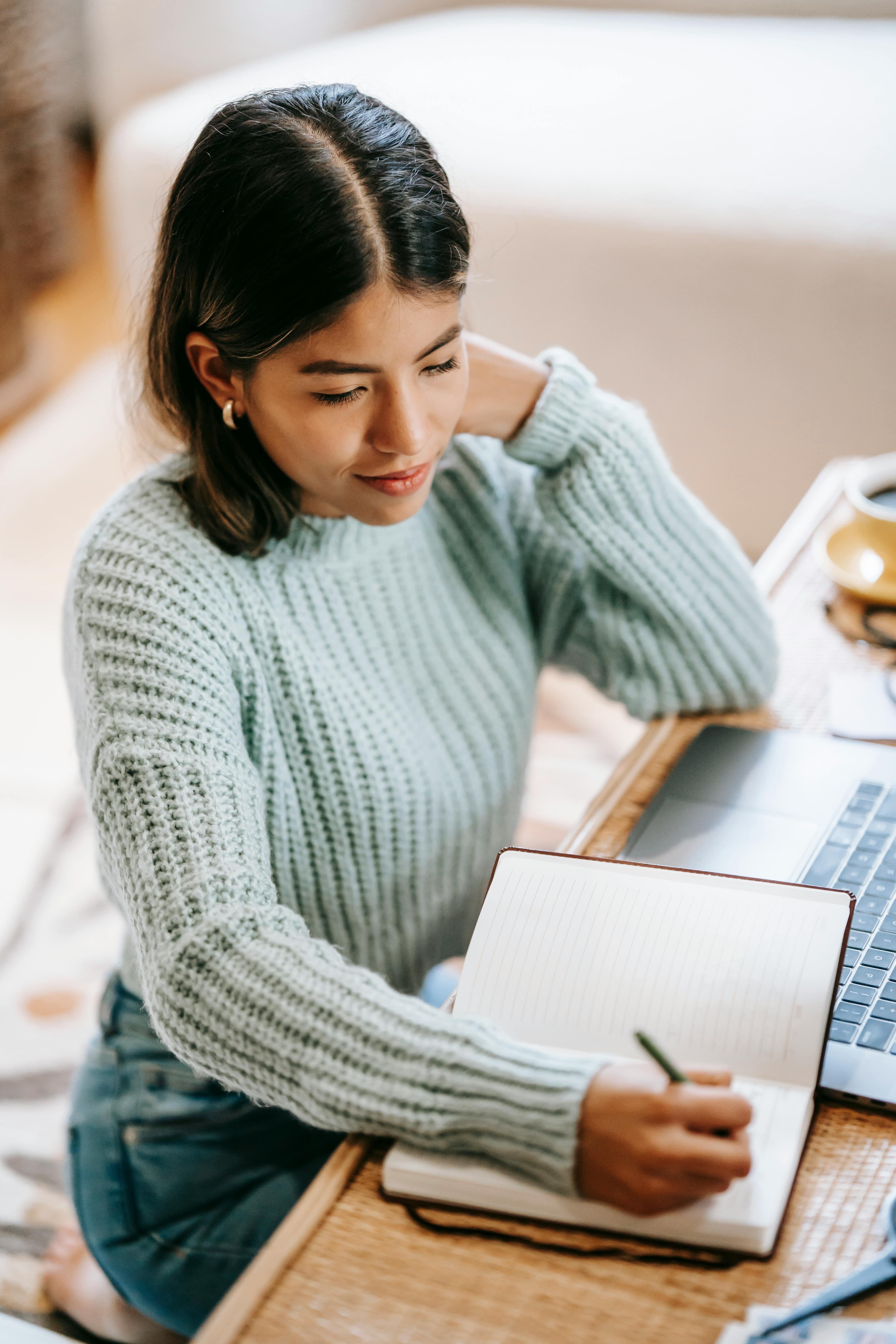 latin american woman taking notes in notebook near netbook