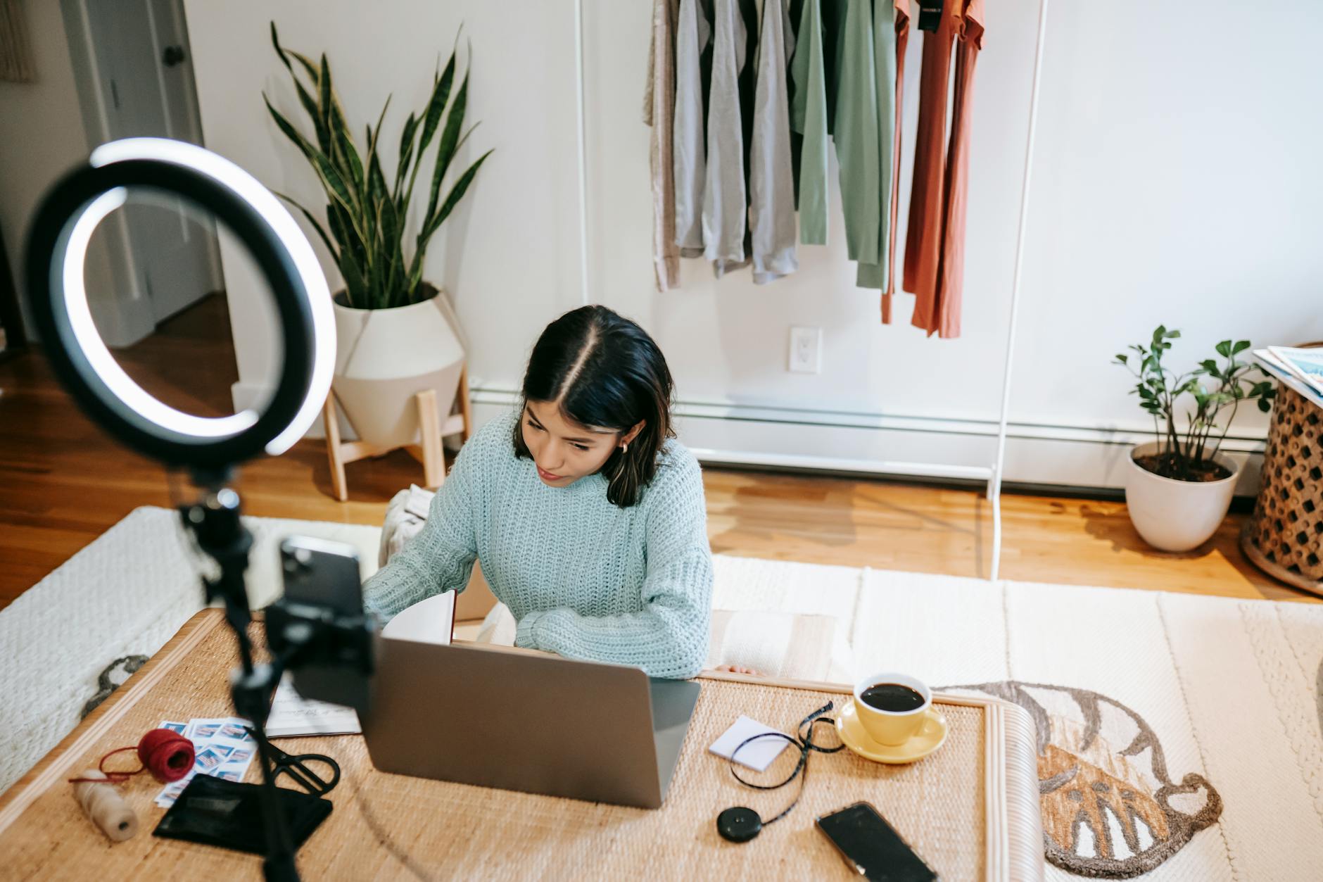 Young woman working at home office with laptop, coffee, and lighting equipment.