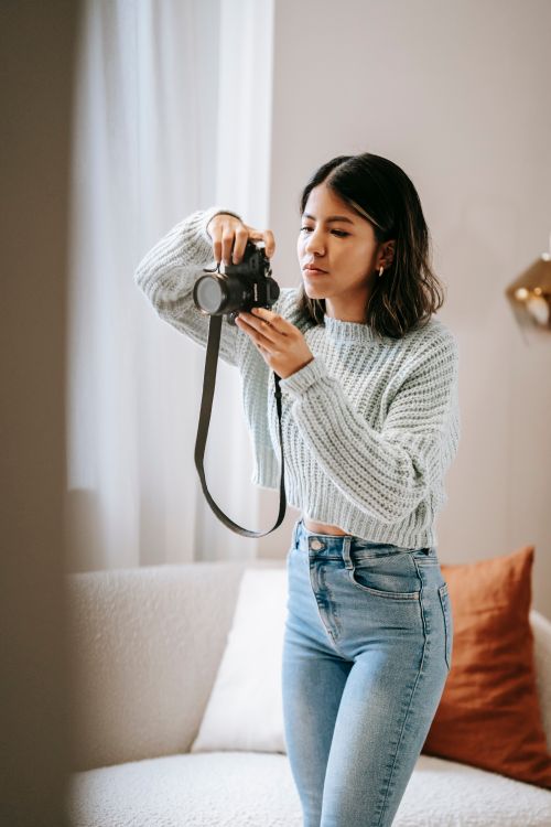 Free Young Latin American woman in casual apparel taking photo on professional camera in living room Stock Photo
