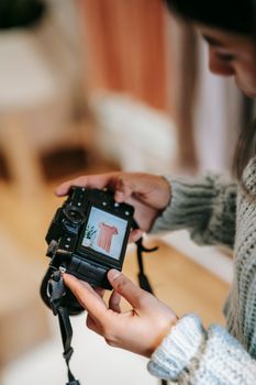 Side view of crop Latin American female watching photo of blouse on digital camera screen in house