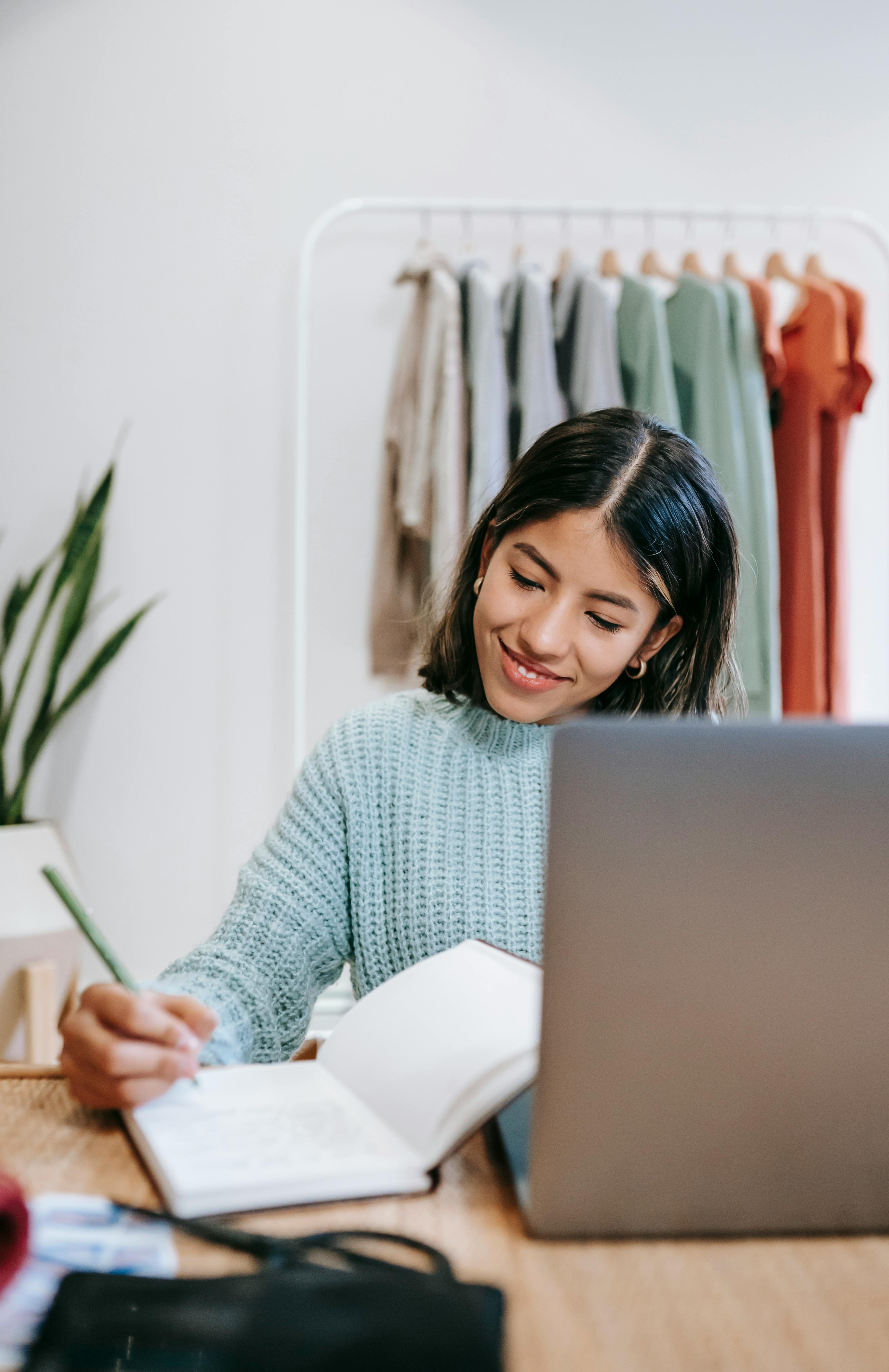 smiling ethnic employee with diary and laptop at home