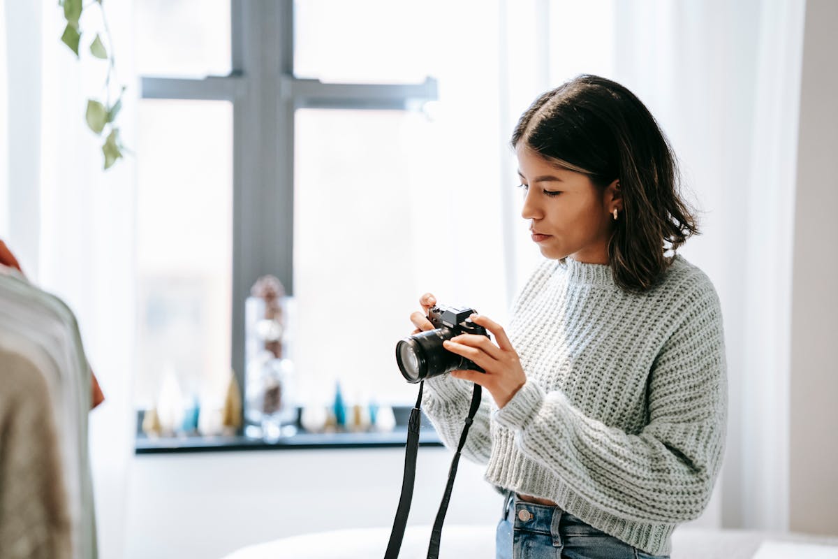 Side view of young Latin American woman taking photo of clothes on camera in house
