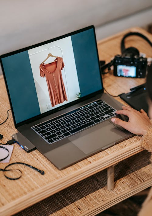 Crop photographer showing photo of blouse on laptop