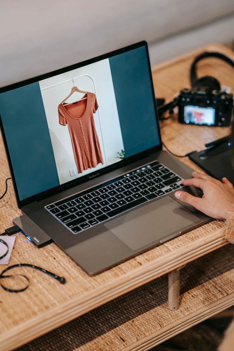 Crop photographer showing photo of blouse on laptop
