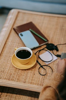 A warm indoor workspace featuring a cup of coffee, smartphone, and notebook on a woven table.