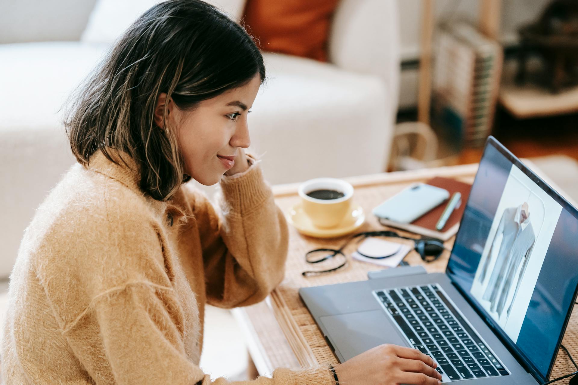 Side view of content Latin American female distance employee working on netbook with photography of shirt on screen at home