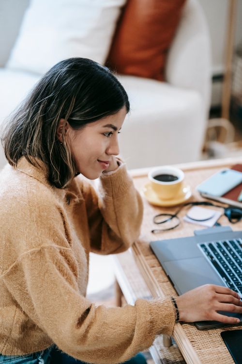 Free Side view of cheerful Latin American female distance worker surfing internet on netbook at table with cup of coffee Stock Photo