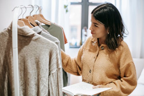 Smiling ethnic designer with notebook against assorted clothes