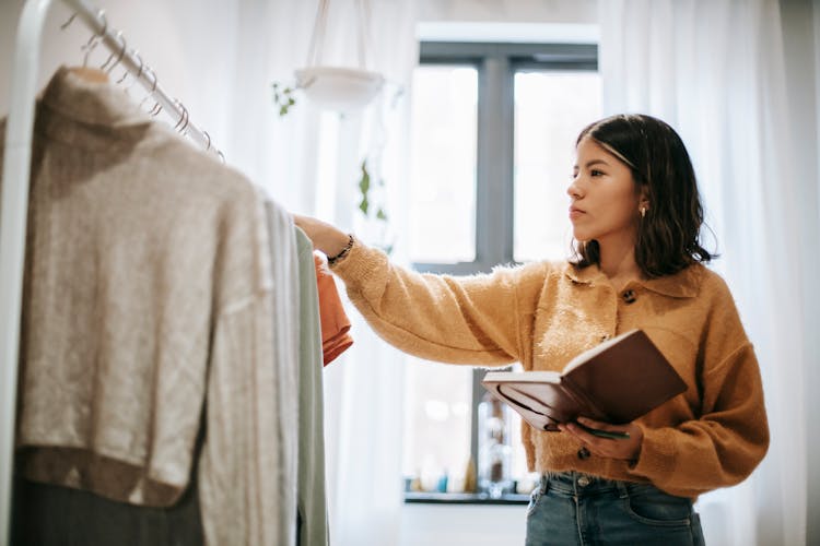 Serious Ethnic Designer Touching Clothes On Rack At Home