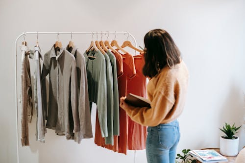 Faceless female seller with notepad near clothes on hangers