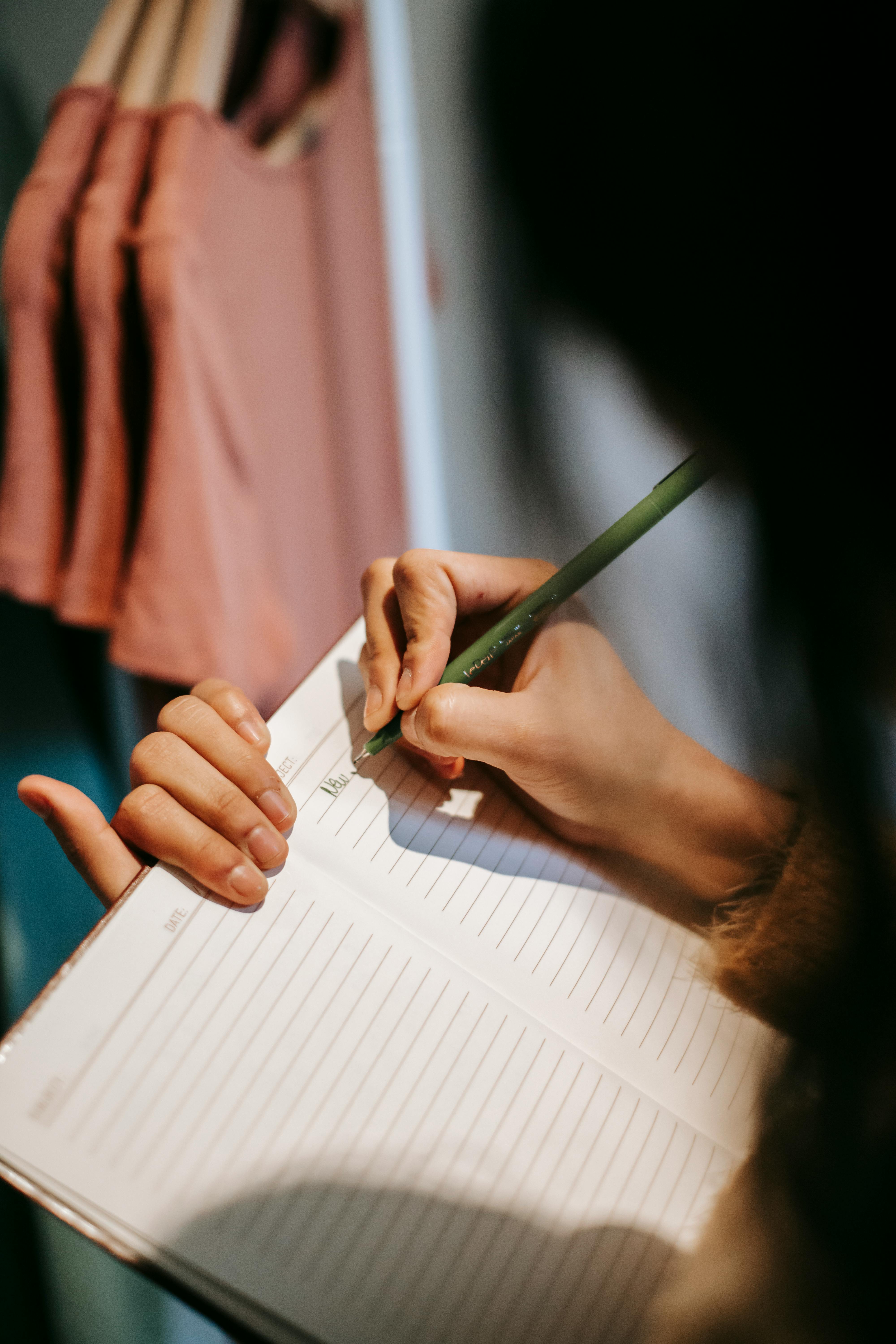 unrecognizable female writing information in notepad near wardrobe in store