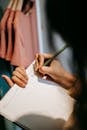 Unrecognizable female writing information in notepad near wardrobe in store